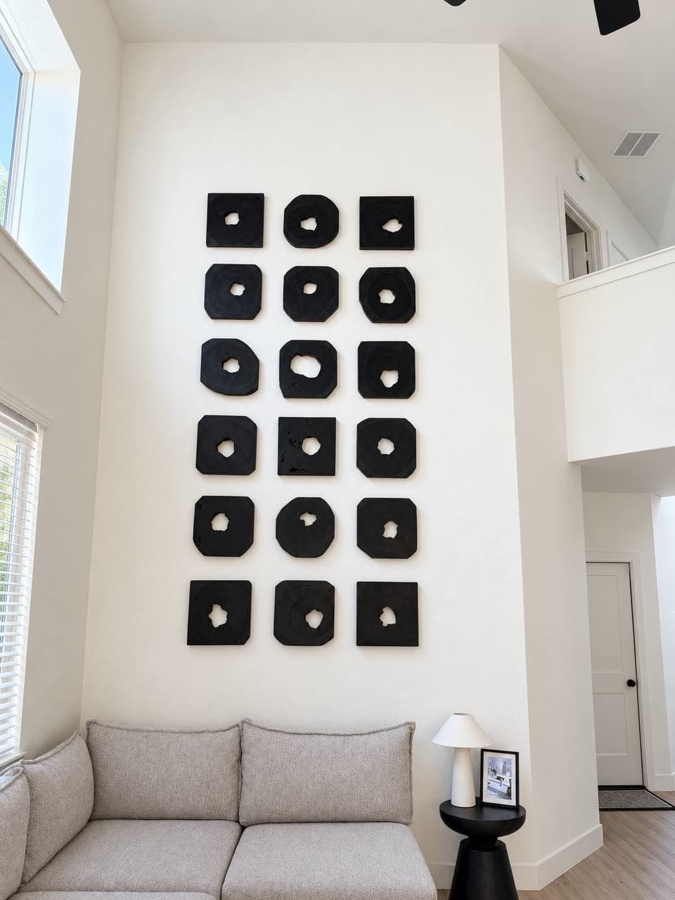 Eighteen black sculptural relief tiles hung as a six-by-three grid on a double-height living room wall.