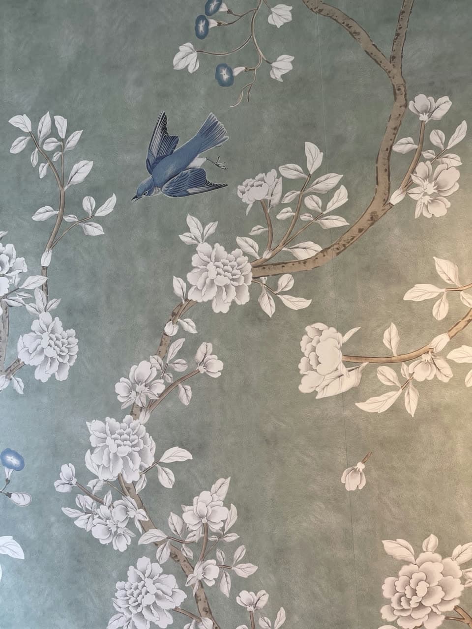 Close view of a hand-painted-look mural — white peonies, blossom branches and a blue bird on a soft grey-green ground.