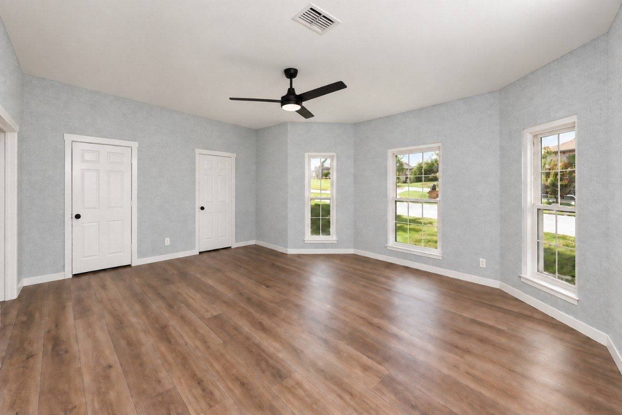 Empty bedroom with pale blue woven-texture wallpaper on all walls, a ceiling fan and three windows.