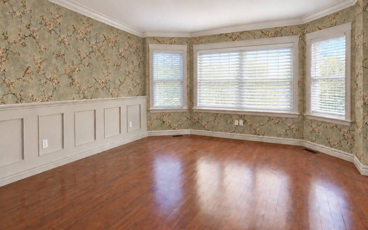 Room papered in a floral and bird pattern above white panel wainscoting, wrapping a bay window.