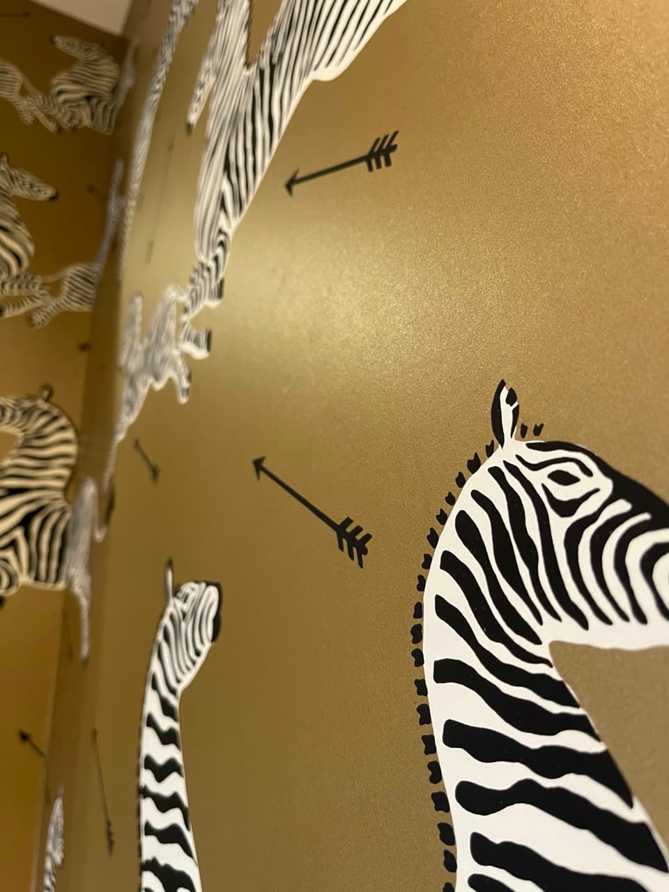 Close view of wallpaper with black and white zebras and arrows on a metallic gold ground, wrapping an inside corner.