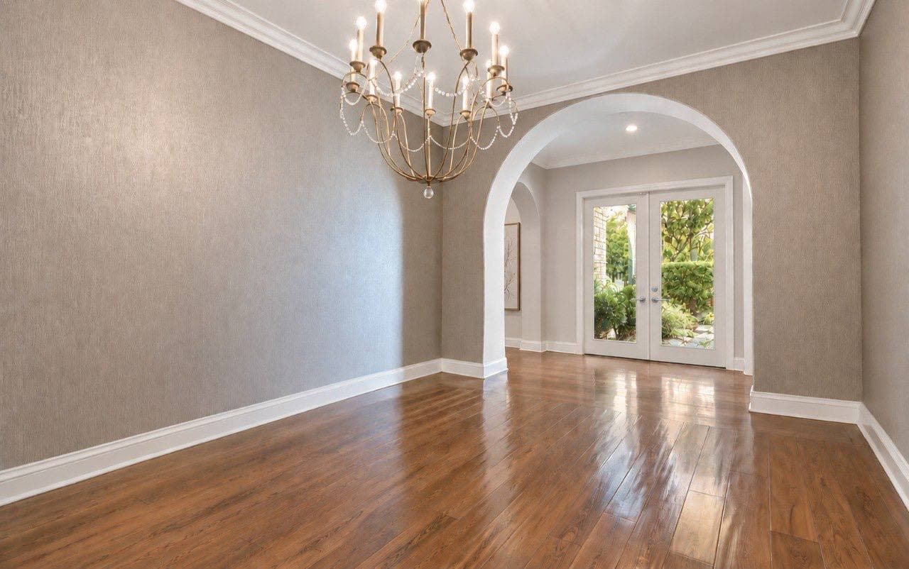 Dining room in taupe grasscloth wallpaper with a beaded chandelier and an arched opening.