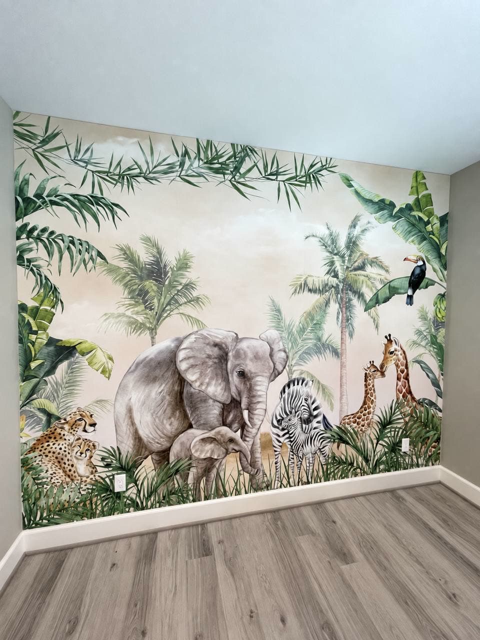 Nursery wall with a watercolour safari mural — elephants, a zebra, giraffes, a cheetah and palms — against a pale blue ceiling.