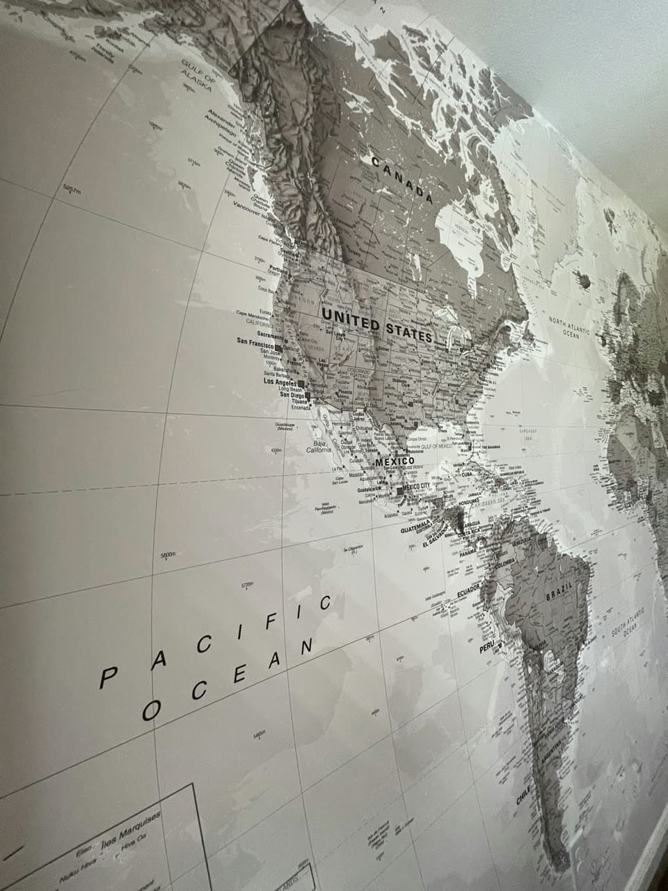 Wall covered by a large grey and white world map mural, photographed at an angle along the wall.